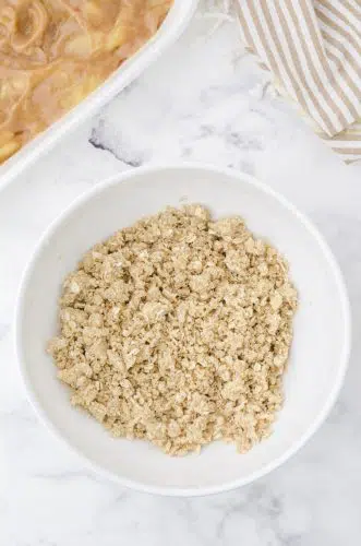 Crumb topping for apple crisp with pie filling in a bowl.