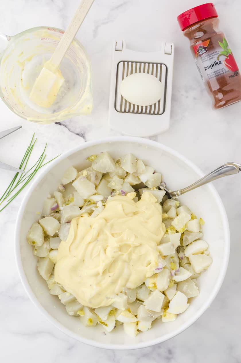 Potato salad dressing being mixed into creamy potato salad recipe in a large white bowl