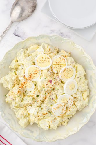 a bowl of potato salad with sliced eggs and paprika on the top for garnish