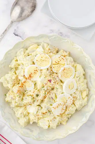 a bowl of potato salad with sliced eggs and paprika on the top for garnish
