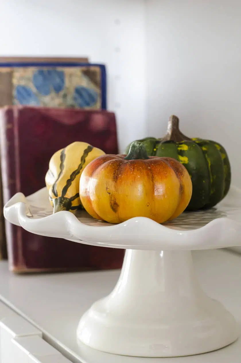 Faux pumpkins piled on a cake stand sitting in a Billy Bookcase as a Fall decor idea
