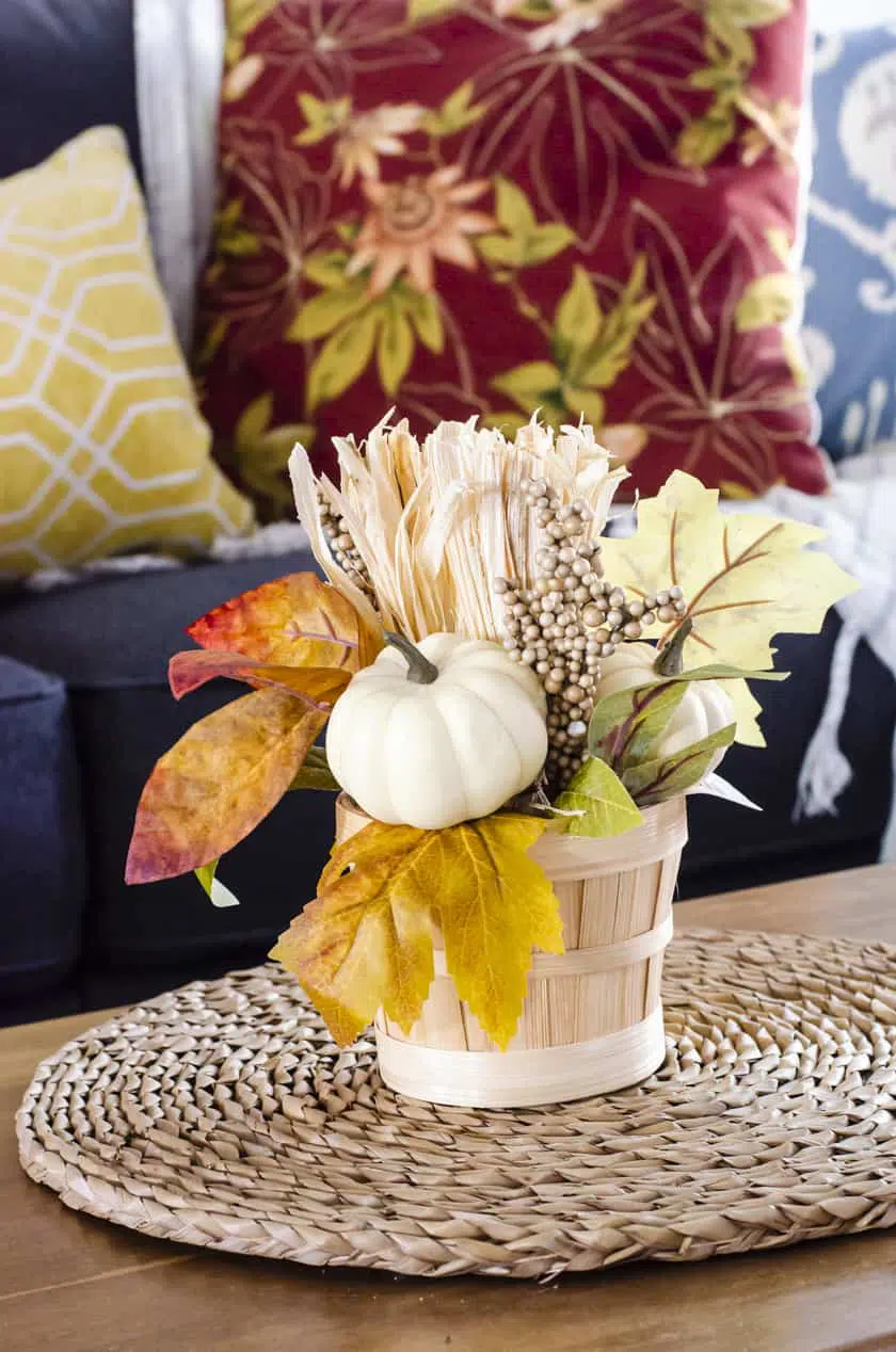 Fall floral arrangement in a basket sitting on a coffee table.
