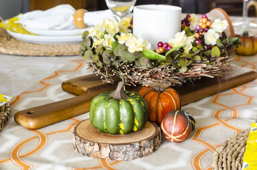A Fall dining room table centerpiece with faux pumpkins beside