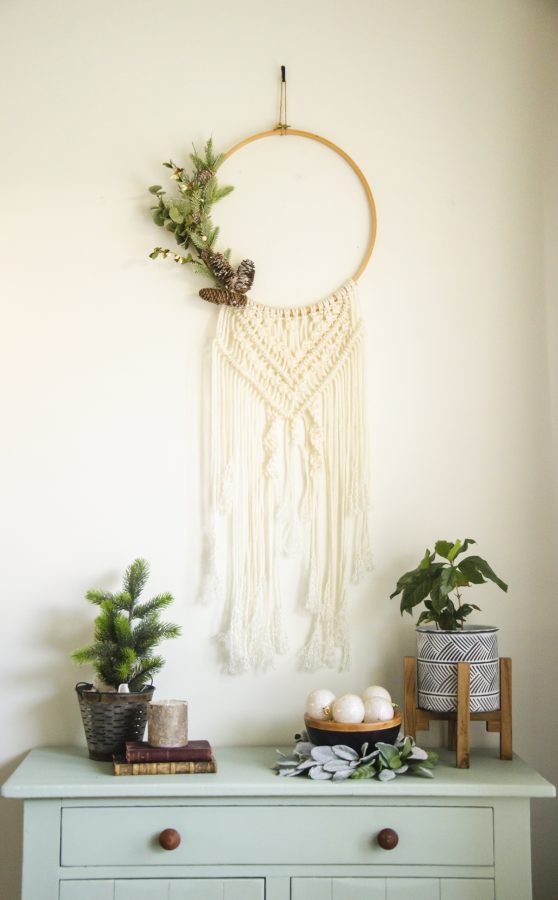 Macrame wall hanging above a green dresser with plants and a bowl of Christmas balls on it.