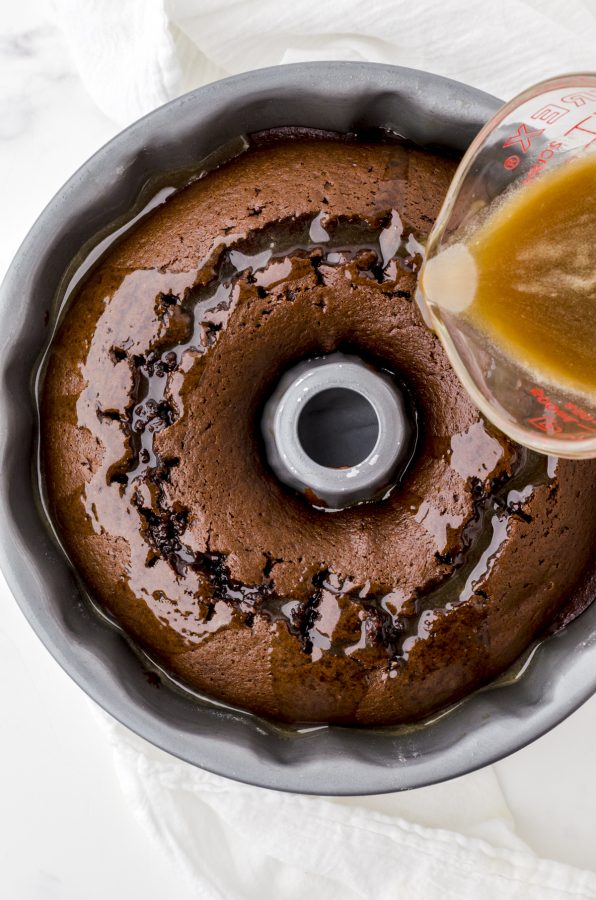 Poke and pour cake sauce being poured onto the top of the gingerbread spice cake in a bundt pan.