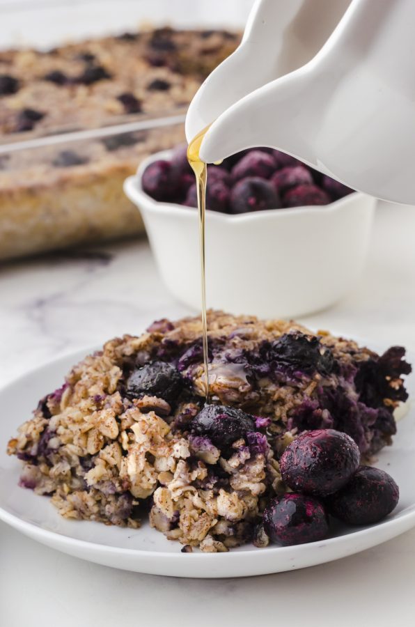 A piece of banana blueberry bake oats on a place with maple syrup being drizzled over the top.