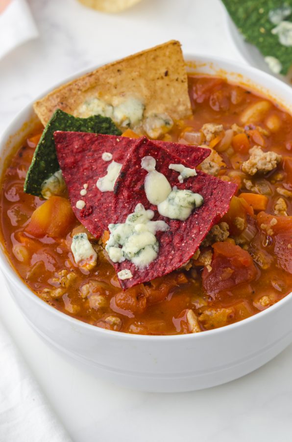 Red tortilla chips with melted blue cheese sitting on top of a bowl of spicy buffalo chicken chili soup.