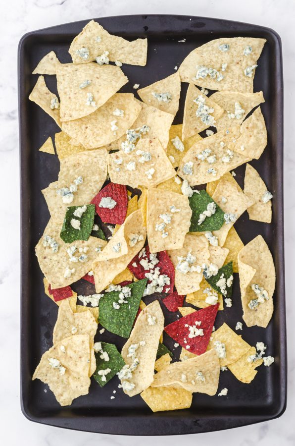 A stoneware baking pan with a layer of colored tortilla chips and crumbled blue cheese on the top.