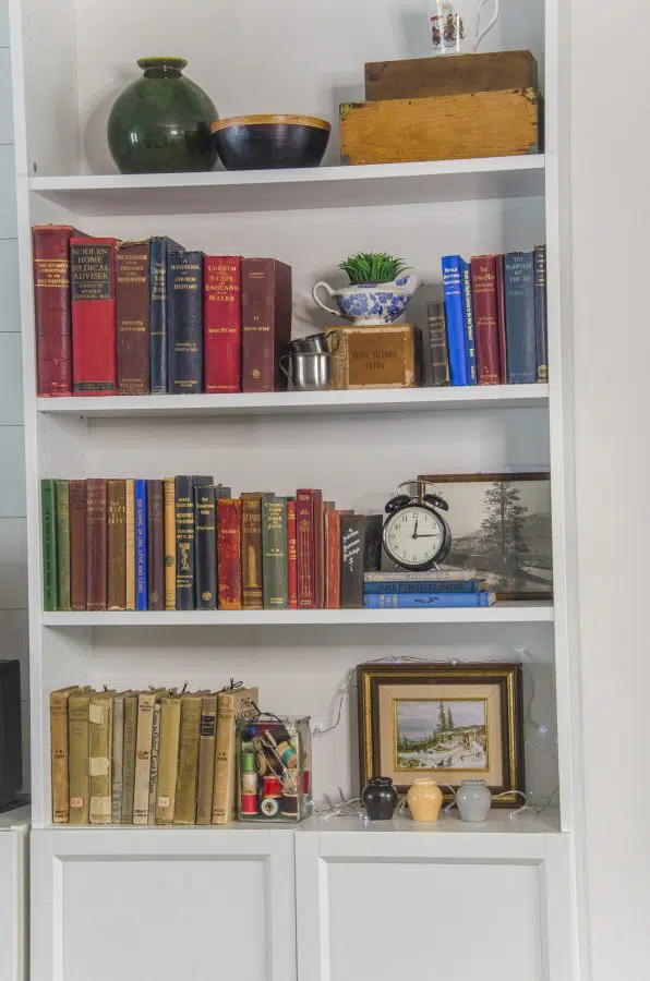 A great way to add style to a cottage core room is to add vintage items to a bookcase - like vintage books, stoneware and fairy lights.