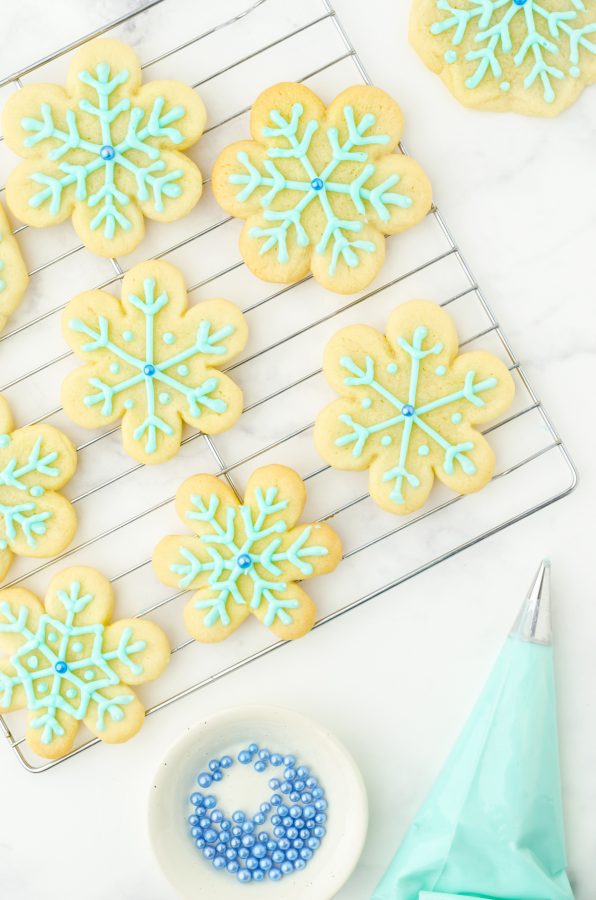Close up of snowflake sugar cookies with blue frosting in a pastry bag.