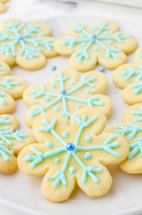 Platter of snowflake cookies made with Pillsbury sugar cookie dough decorated with blue icing and blue pearl sugar bead in the center