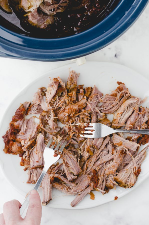 Pork being shredded with 2 forks on a plate for this easy pulled pork recipe