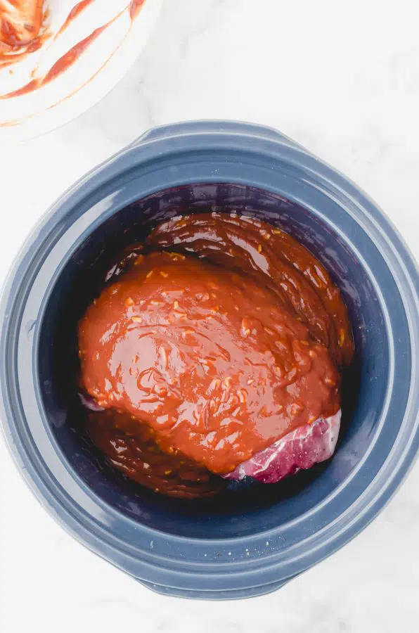Sauce poured on top of a pork roast in a crock pot for this easy pulled pork crock pot recipe