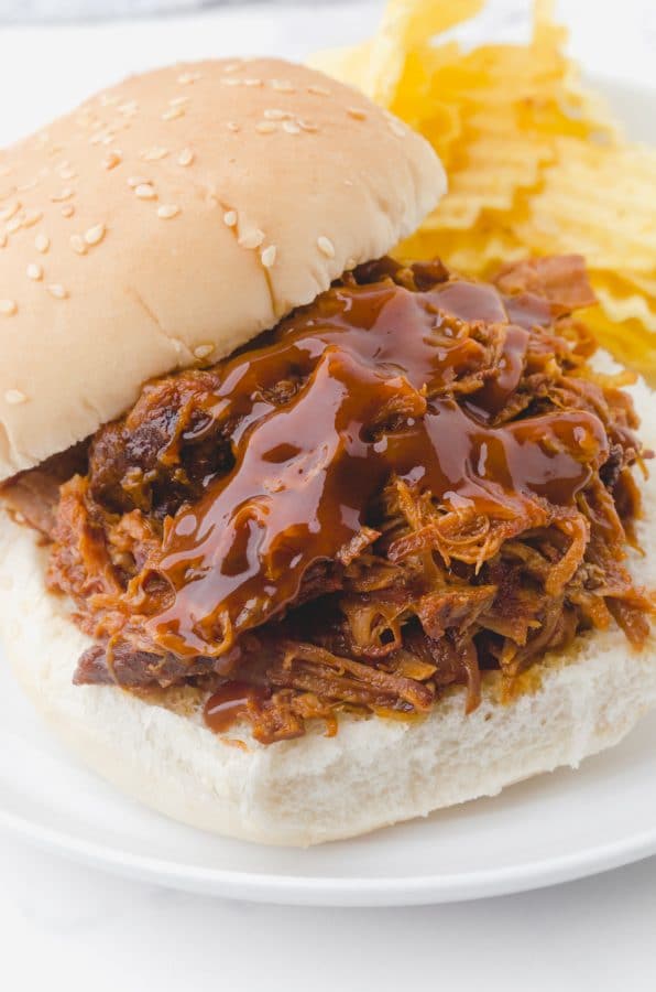 Crock pot pulled pork piled on a bun and topped with a drizzle of bbq sauce.
