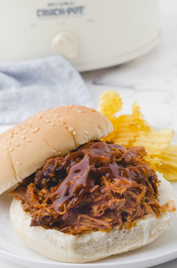 A pulled pork sandwich with barbecue sauce drizzled on the top of the meat.