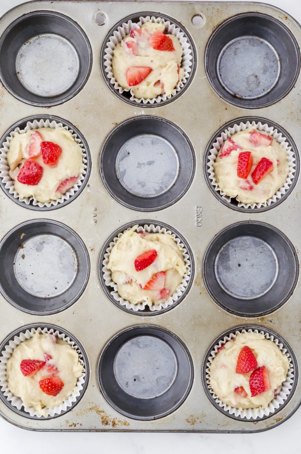 Strawberry muffins batter in a muffin tin with every other hole empty.