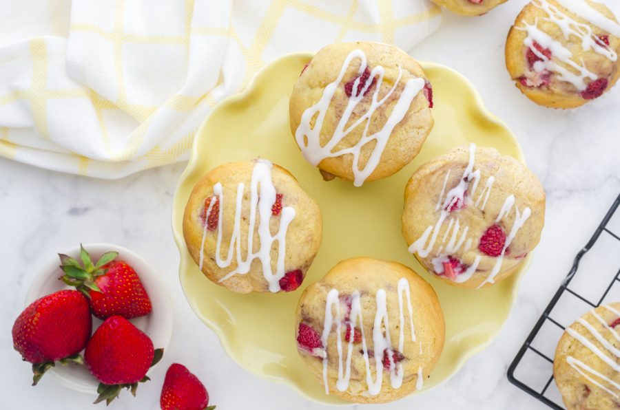 A yellow platter with strawberry muffins on it with a pile of fresh strawberries on the side.