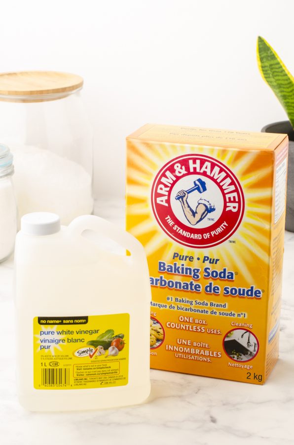 A boc of baking soda and container of white vinegar sitting on a counter.