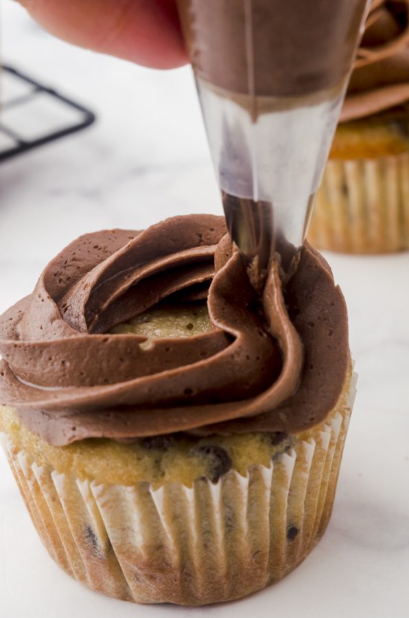 Icing being piped in a circular motion from outside edge of the cupcake, making smaller overlapping circles toward the center.