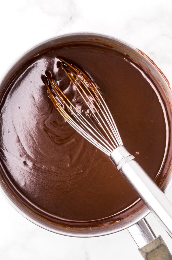 Finished homemade hot fudge sauce in a saucepan with a whisk sitting in it.