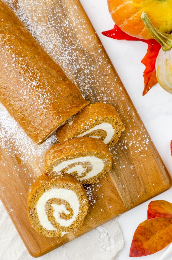 Pumpkin Roll Cake sliced on a wooden cutting board and sprinkled with sugar.