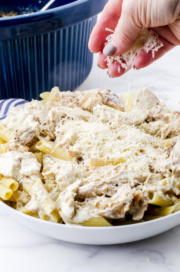 Slow cooker chicken alfredo in a serving bowl with cheese being sprinkled on the top.