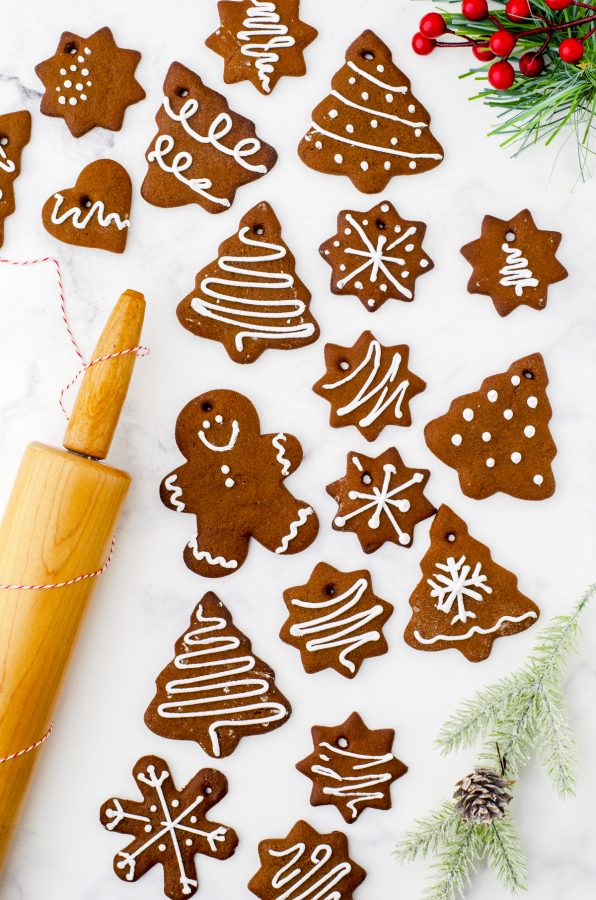 A variety of gingerbread cookies laying on a marble surface with a rolling pin beside.