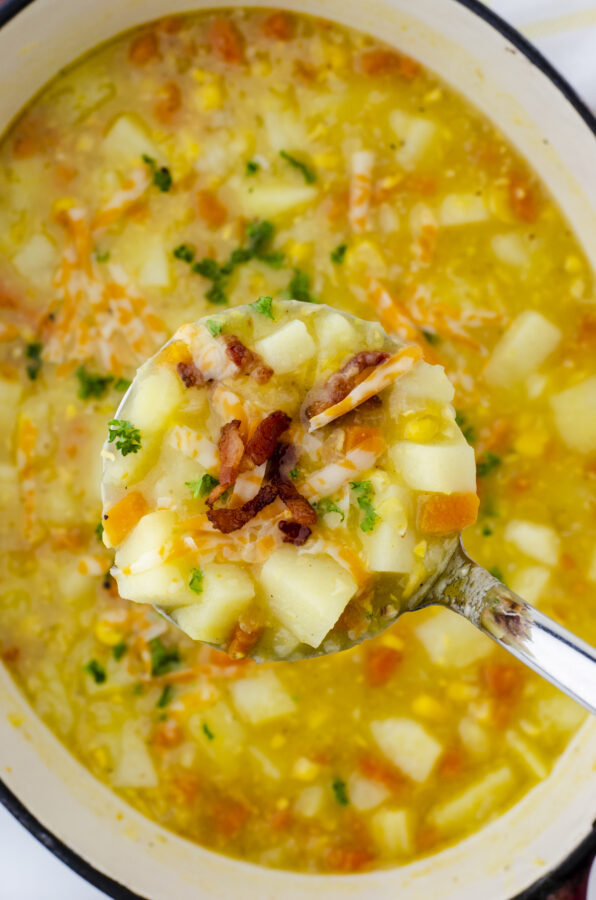 A ladle full of hearty, chunky potato soup with bacon bits and shredded cheese.