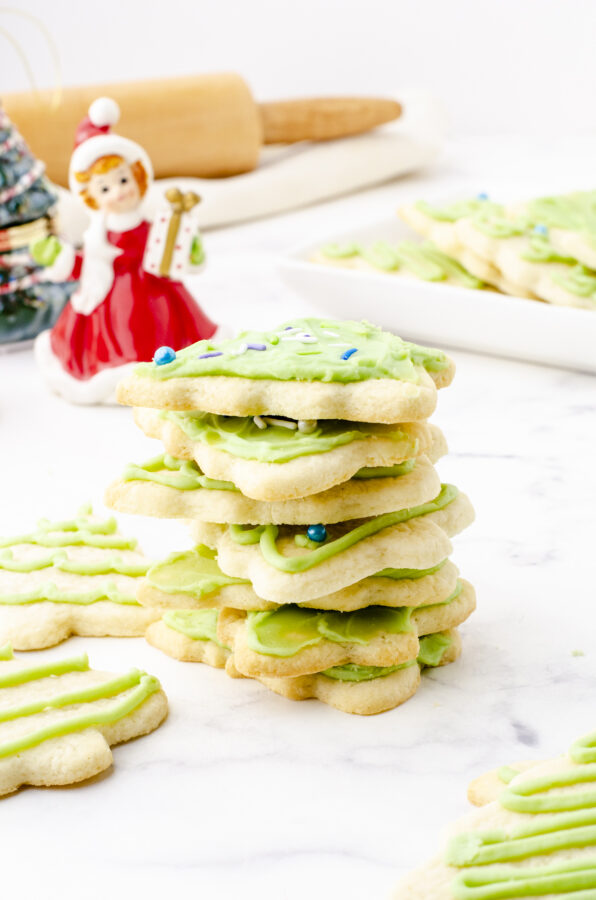 A stack of rolled sugar cookies with a rolling pin and pastry cover in the background.