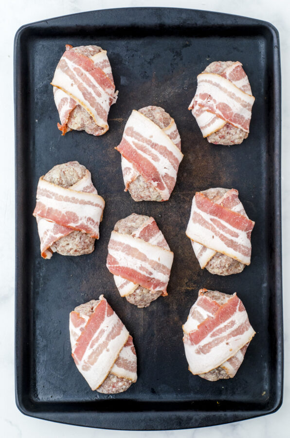 Bacon wrapped meatloaf in mini individual portions arranged on a baking pan ready to go into the oven.