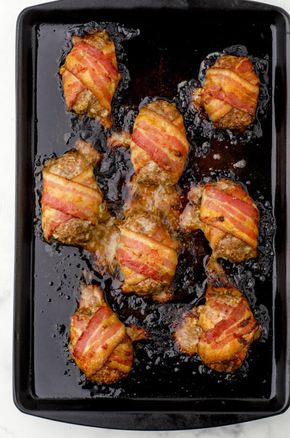 Baked mini bacon wrapped meatloaf portions on baking sheet right after being pulled from the oven.