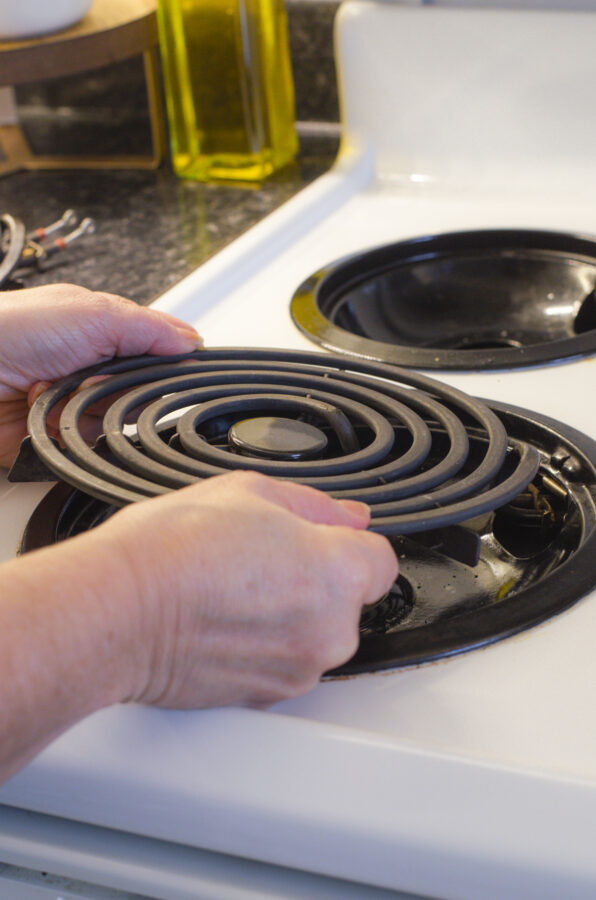 Woman removing cold electric stovetop coils in preparation for cleaning the electric stovetop.
