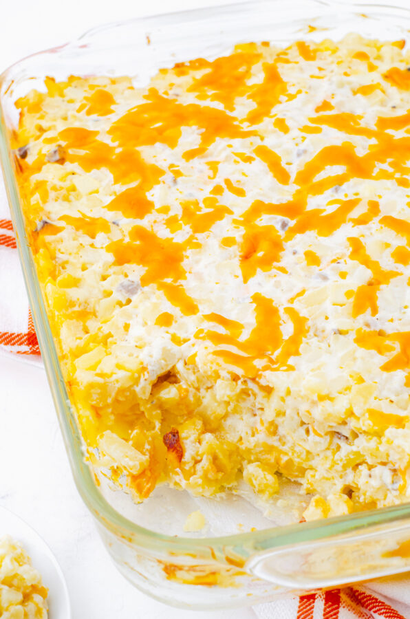 Baked cheesy potatoes casserole with hashbrowns with a serving dished out of the casserole dish.