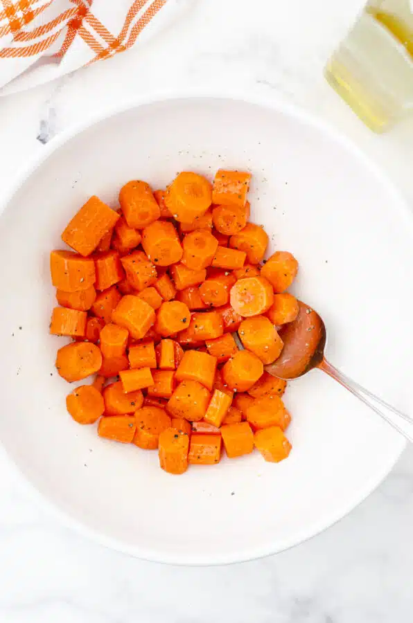 Carrot chunks in a large mixing bowl with olive oil and salt and pepper.