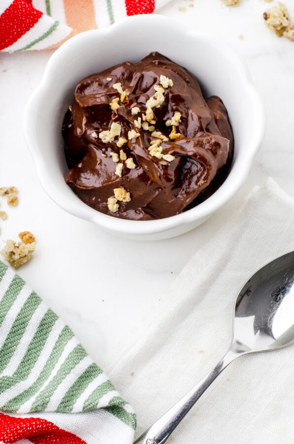 a bowl of chocolate avocado pudding with granola sprinkled on the top.