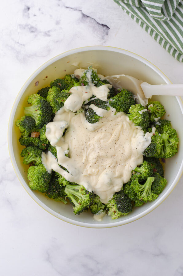 Dressing being mixed into a bowl of broccoli salad with cranberries and bacon