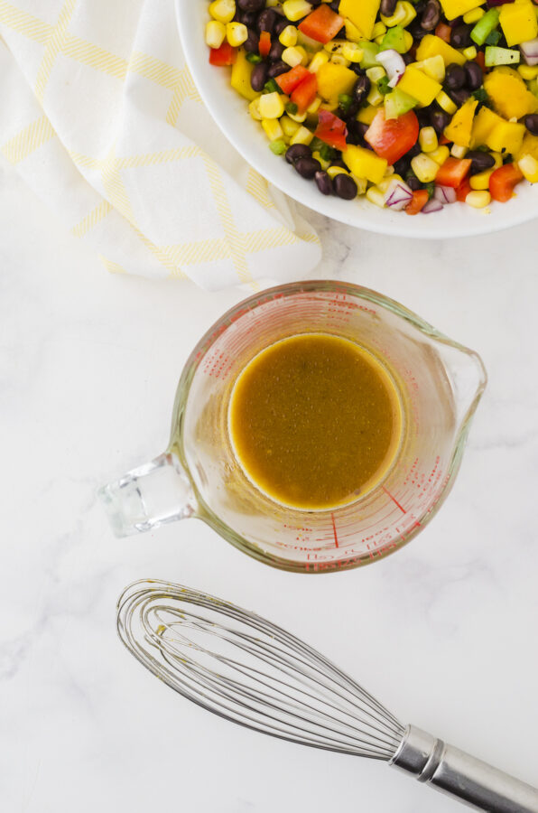 Mango salad dressing whisked together in a large measuring cup that pours.