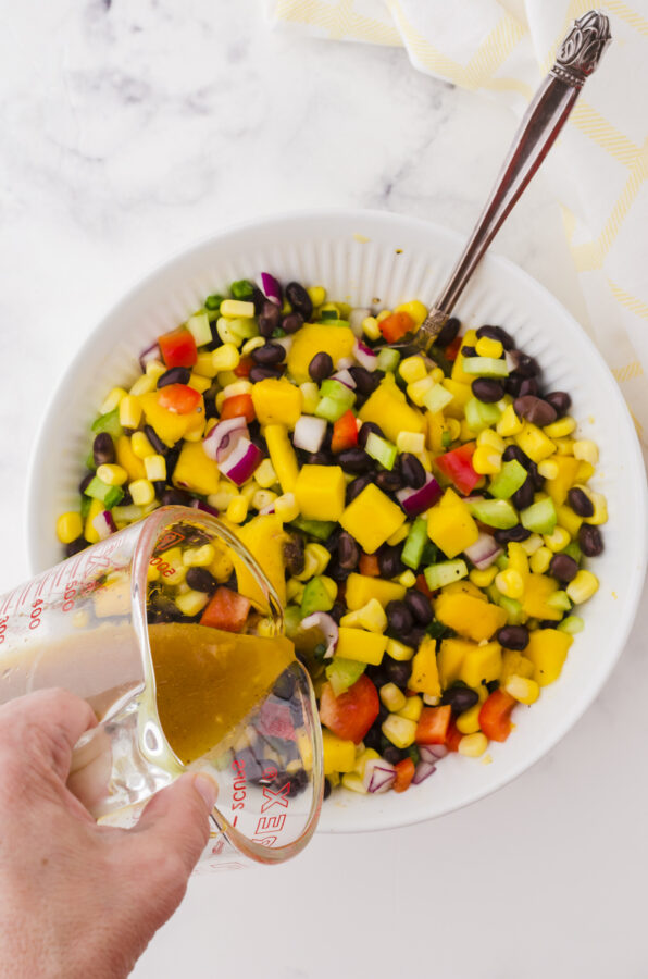 Mango salad dressing being poured on a bowl of mango salad.