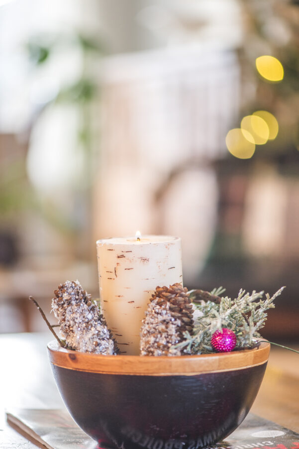 a wooden bowl with a candle and pine cones around it