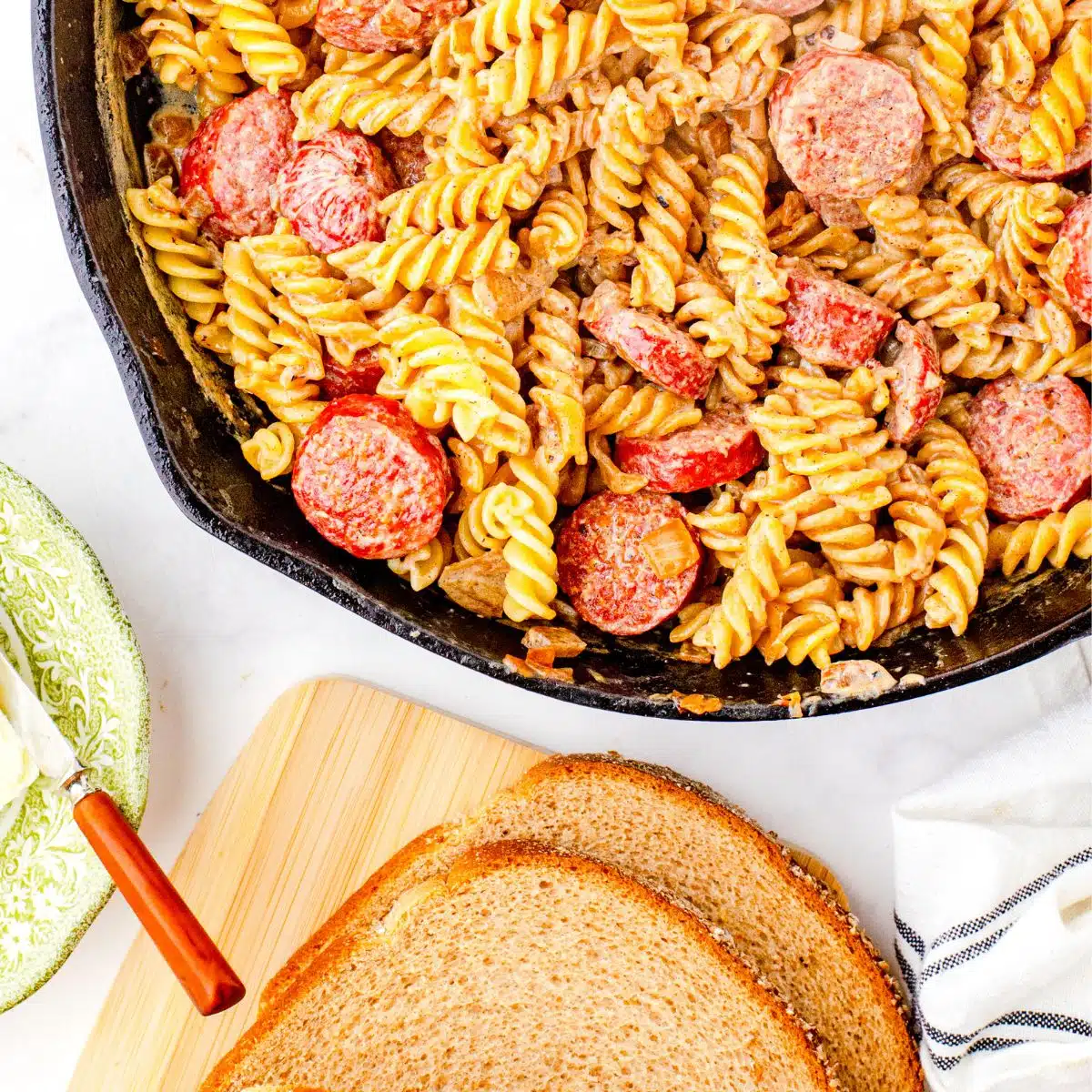 Farmers sausage and noodles recipe in a cast iron skillet with bread and butter on the side