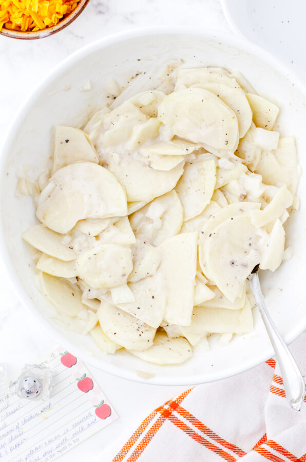 Scalloped potatoes with mushroom soup sauce stirred together in a large bowl.