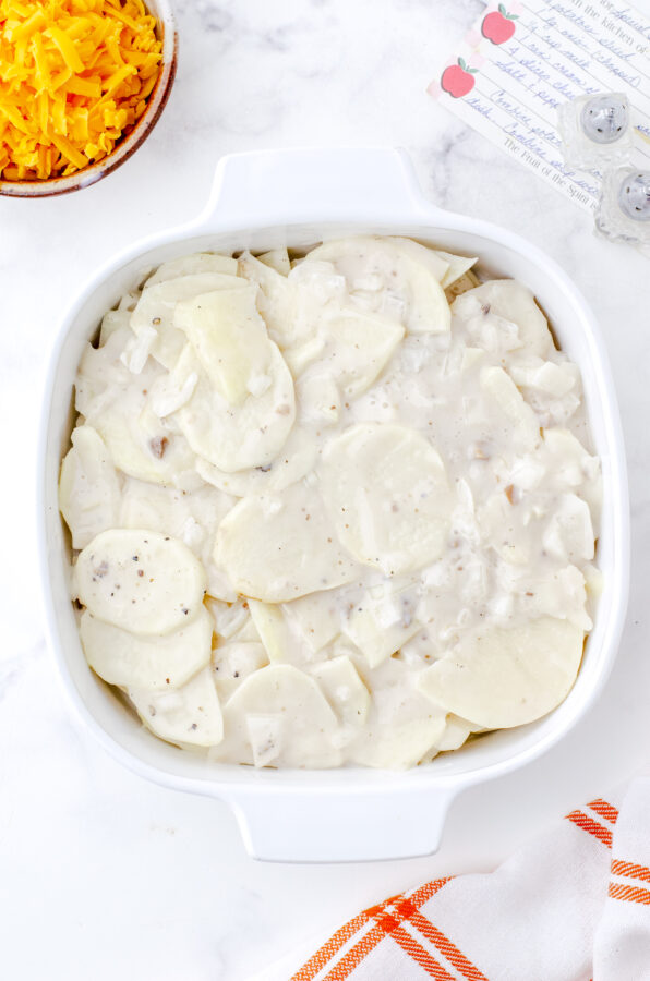 Scalloped potatoes and mushroom soup sauce in a square casserole dish ready to be put in the oven.
