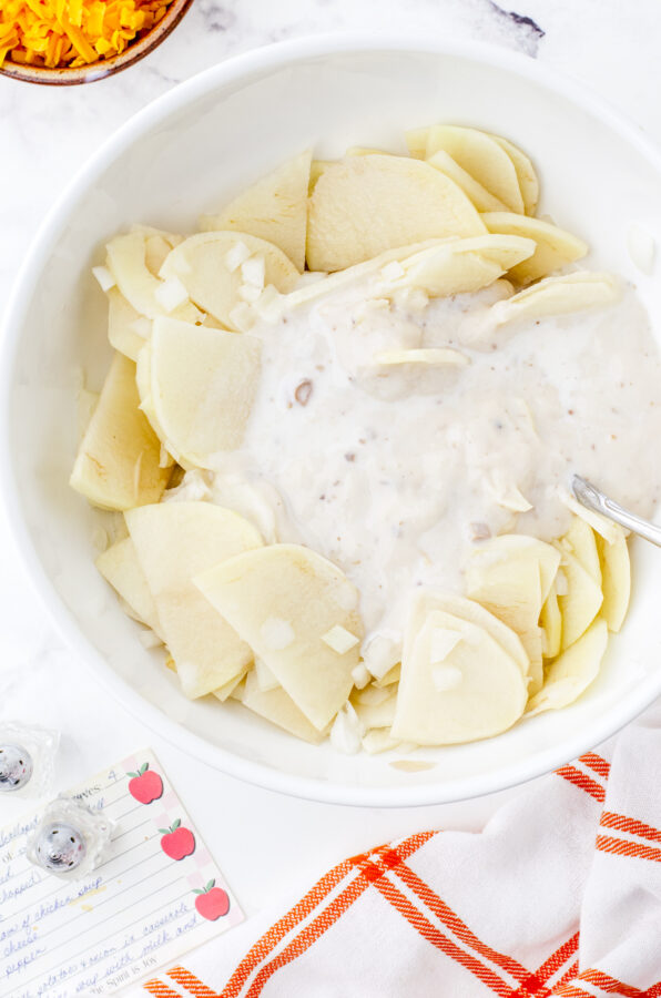 Mushroom soup sauce poured on top of sliced potatoes in a large bowl for scalloped potatoes recipe.