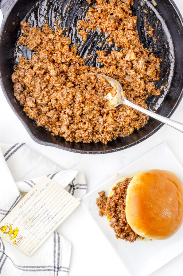 A pan of sloppy joes meat mixture with a sloppy joe in a bun on a plate in front of it.