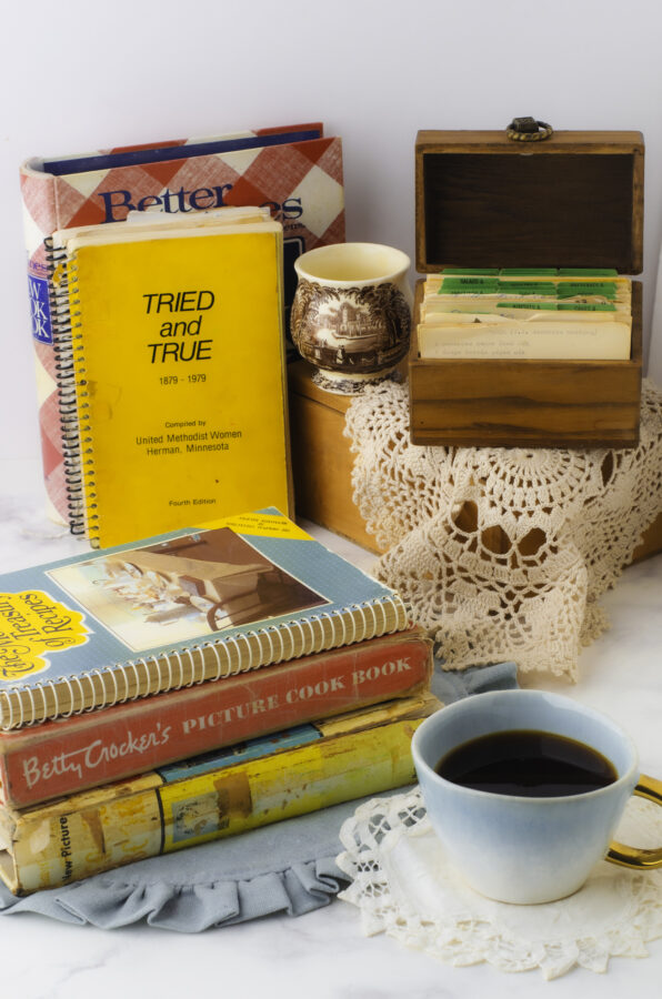 Collection of the best vintage cookbooks stacked up with old recipe cards beside them.