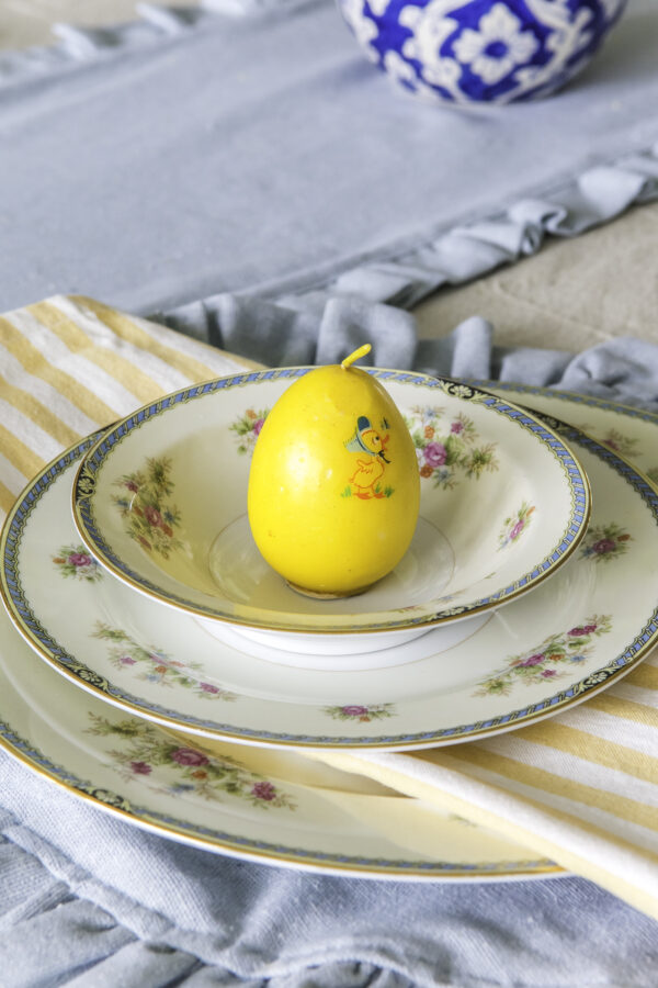 A table setting with vintage china, a yellow striped cloth napkin, and a yellow egg candle on the top plate.