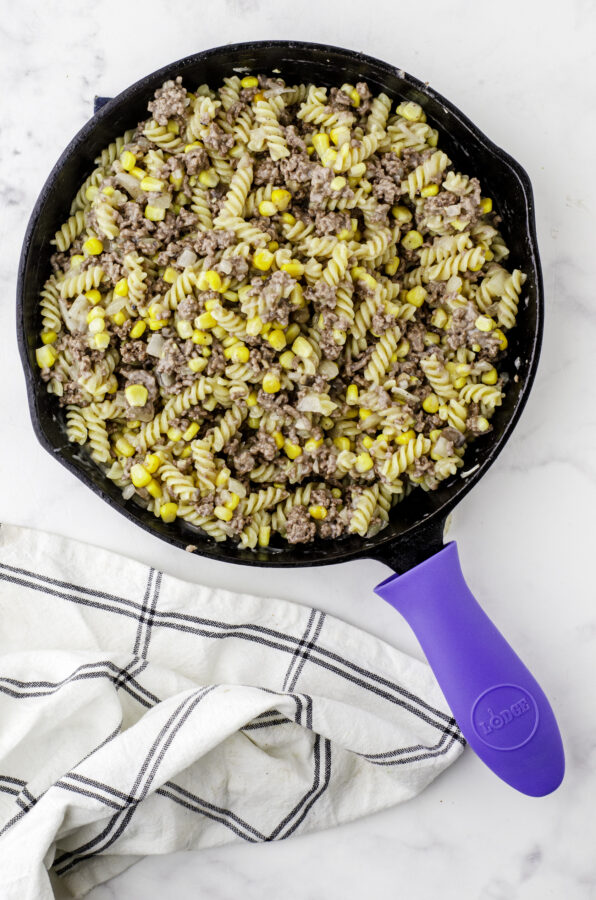 Ingredients stirred together to make hamburger helper beef strognaff in a cast iron skillet.