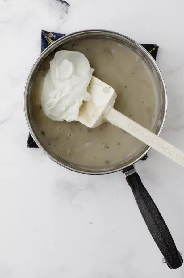 Sour cream being stirred into a saucepan of warm mushroom soup