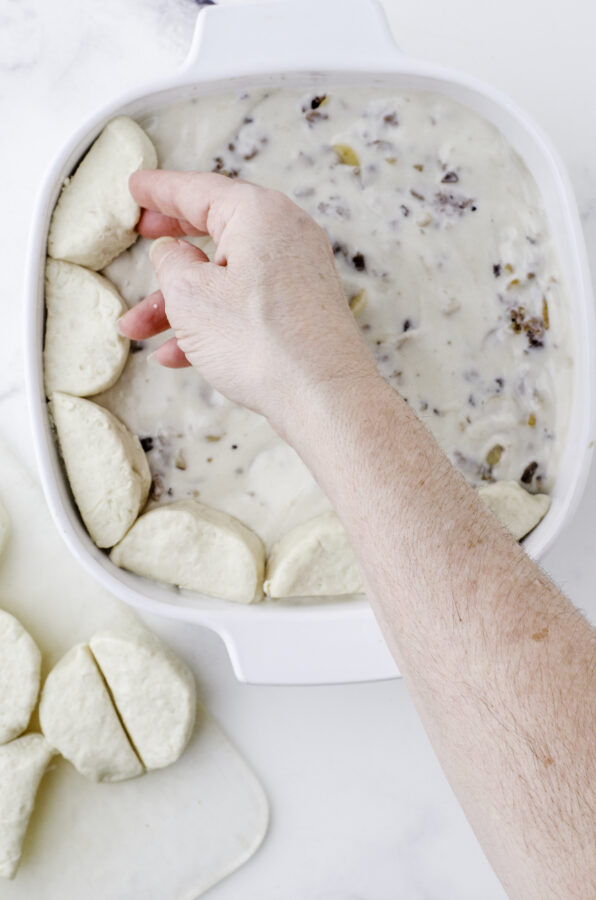 Canned biscuits being arranged around the edge of a casserole dish on top of the hamburger stroganaff mixture