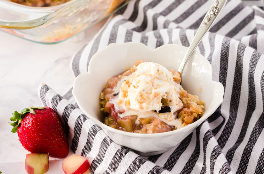 A bowl of rhubarb crisp with a scoop of vanilla ice cream on it.